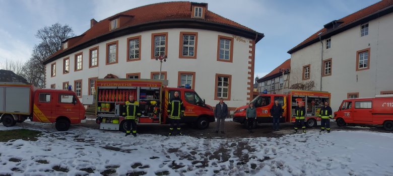 Vertreter von Stadt und Feuerwehr vor den alten und neuen Feuerwehrfahrzeugen und dem Rathaus im Hintergrund