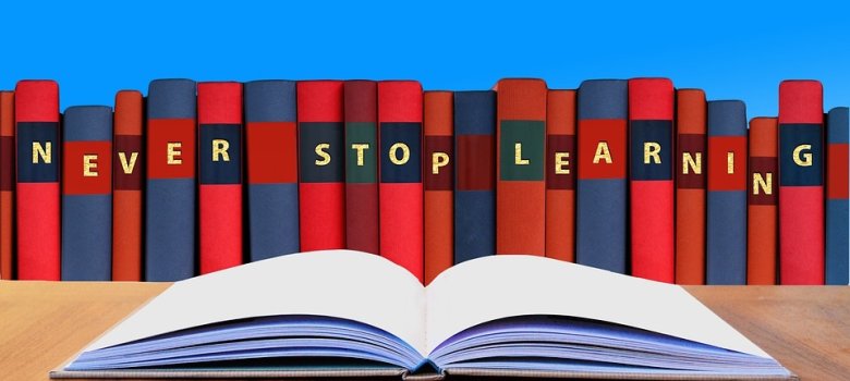 aufgeschlagenes buch auf einem Tisch, im Hintergrund Bücher mit dem Titel Never Stop Learning.jpg