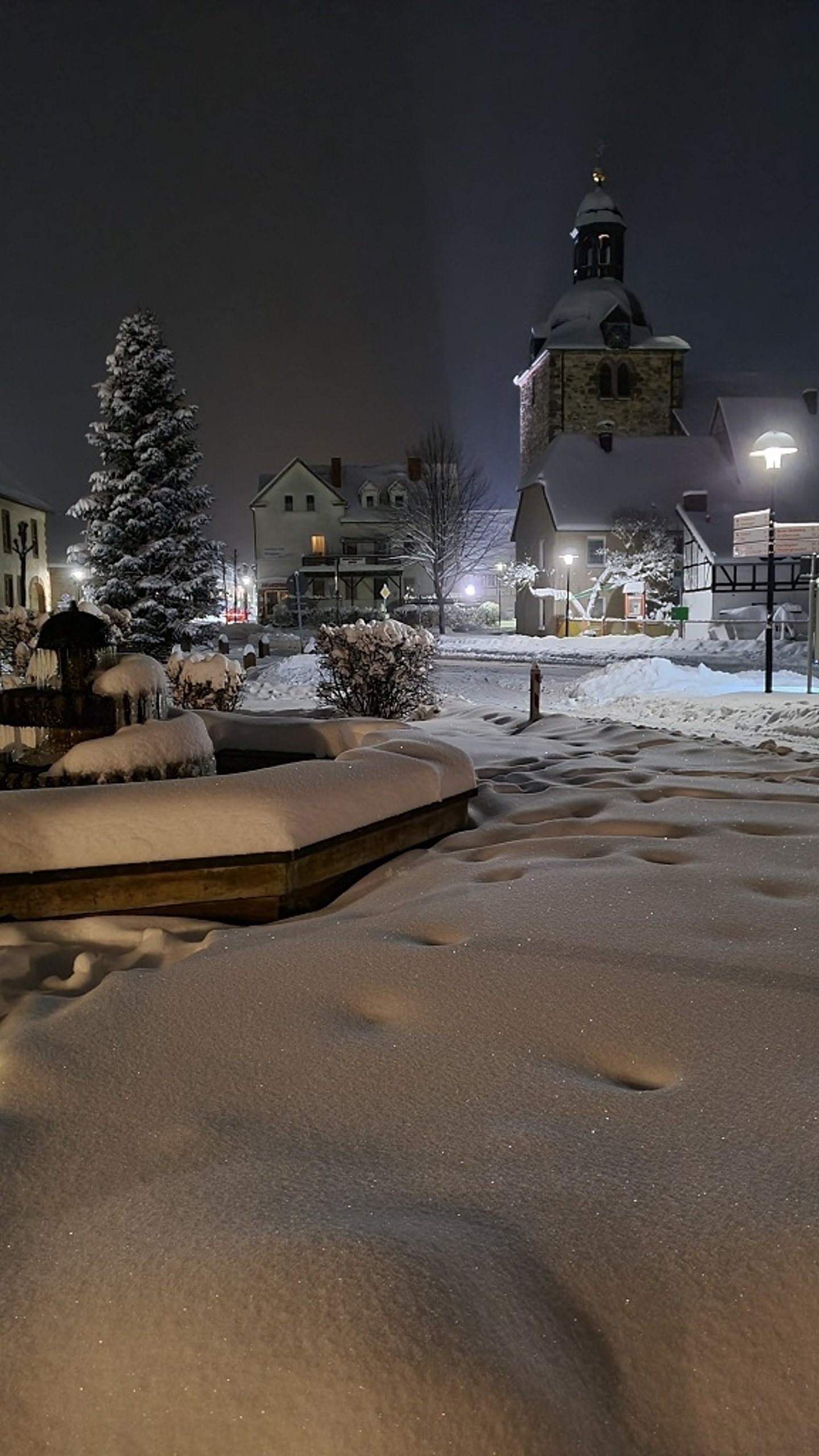 Ein Winterfoto von dem verschneiten Brunnen vor dem Rathaus und der Kirche im Hintergrund