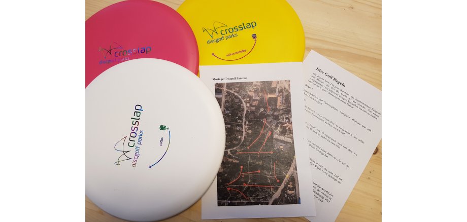 Auf dem Foto sind drei verschiedene Disc Golf Scheiben und eine Anleitung abgebildet